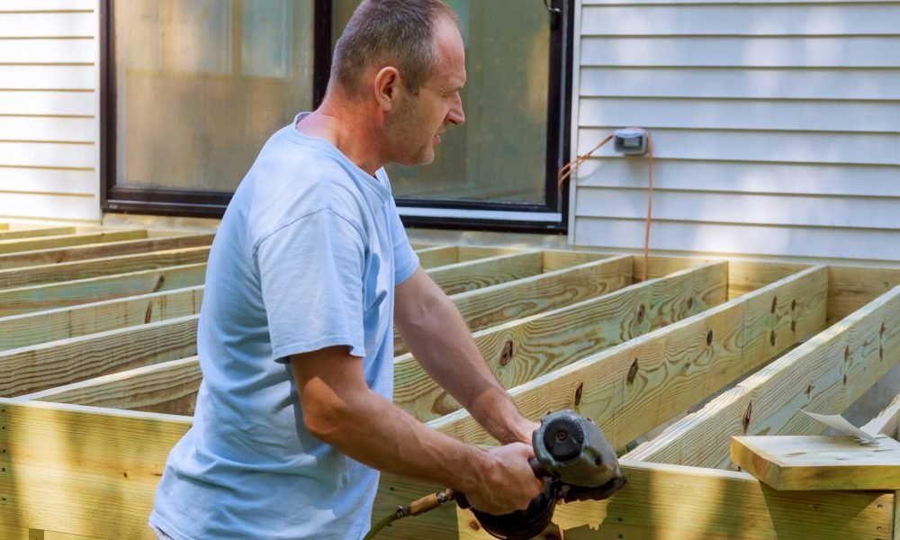 Installing of wooden deck patio carpenter hammering on a deck patio