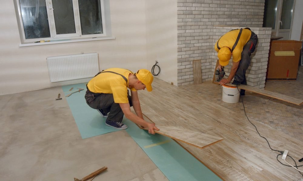 Male worker installing new wooden laminate flooring. Two builders laying laminate wood panel flooring in a house.