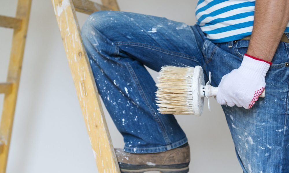 Detail of man painting the walls of new home with paintbrush
